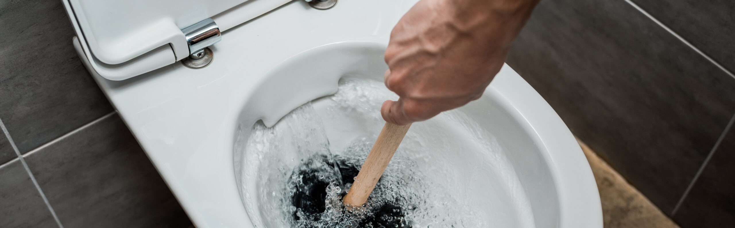 cropped view of plumber using plunger in toilet bowl during flushing in modern restroom